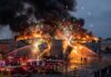Firefighters battling a large industrial fire with explosions and smoke