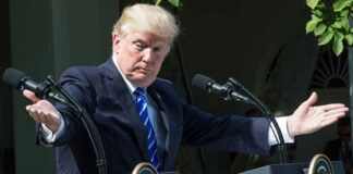 Man speaking at a podium, arms extended outward.