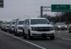 A convoy of white SUVs on a highway with a restricted access sign