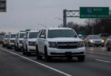 A convoy of white SUVs on a highway with a restricted access sign