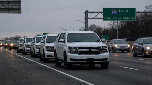 A convoy of white SUVs on a highway with a restricted access sign