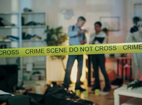Crime scene tape in front of investigators and forensic unit.